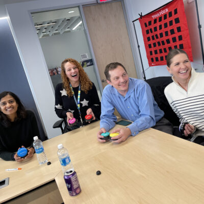 A group of colleagues smiling and engaging in a fun game during a team building event, with colored buzzers in hand and a target game board in the background. thumbnail