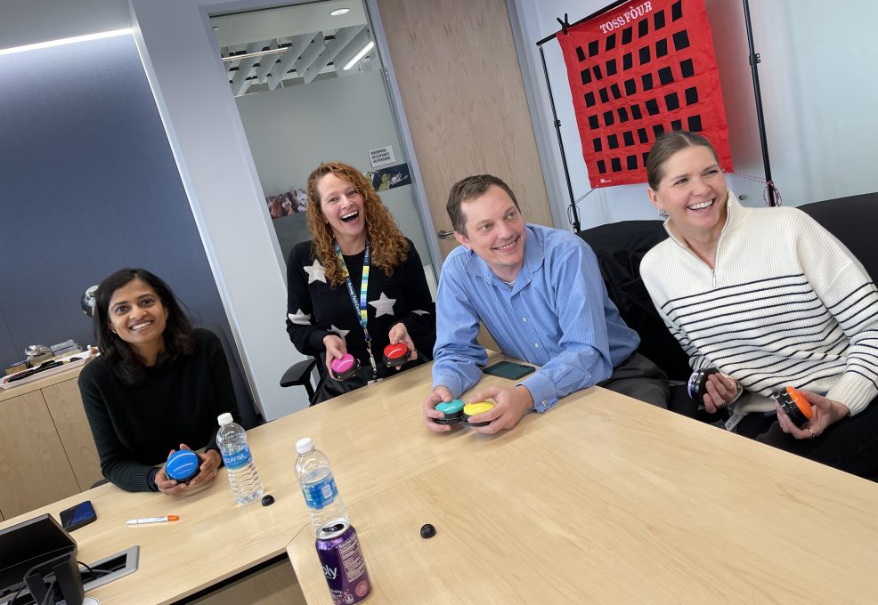 A group of colleagues smiling and engaging in a fun game during a team building event, with colored buzzers in hand and a target game board in the background.