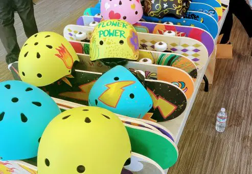 Colorful skateboards and helmets decorated for a charitable team building event. Participants design and assemble skateboards to be donated to children's charities, promoting creativity, teamwork, and community impact.