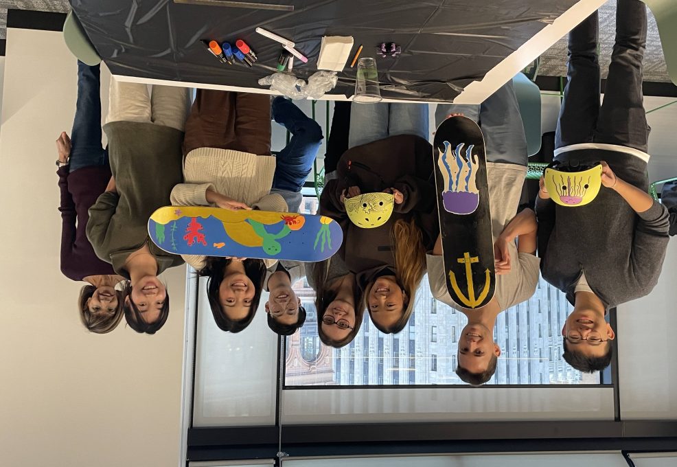Team showcasing their hand-painted skateboards and helmets during a charitable team building event. Participants collaborated to design and assemble skate gear for donation, fostering creativity, teamwork, and community giving.