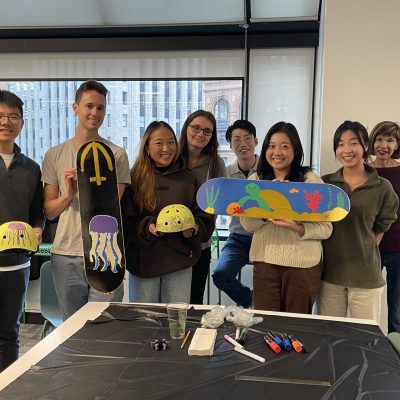 Team showcasing their hand-painted skateboards and helmets during a charitable team building event. Participants collaborated to design and assemble skate gear for donation, fostering creativity, teamwork, and community giving. thumbnail