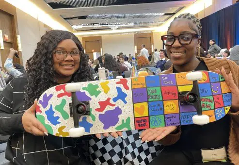 Two participants proudly display their colorful and creatively decorated skateboard, made during the Just Roll With It charitable team building event.