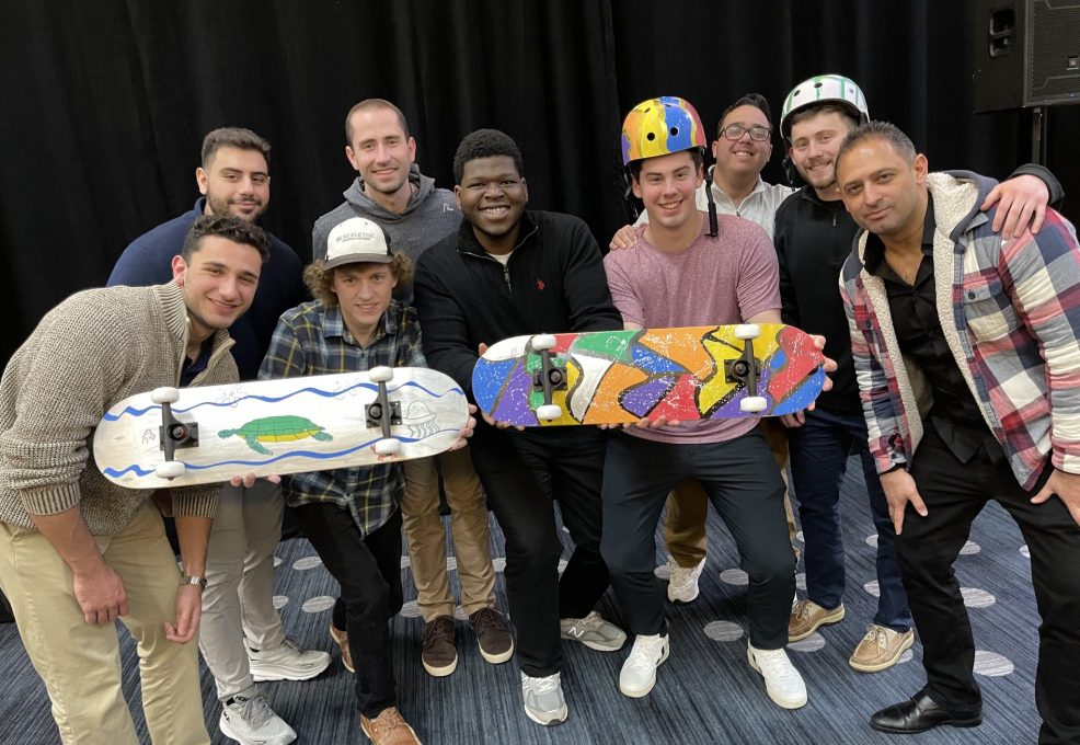 A team proudly showcasing their custom-designed skateboards and helmets created during the Just Roll With It – Charitable Skateboard Build team building event.