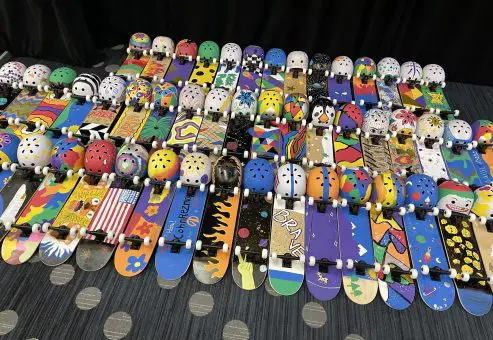 A vibrant display of decorated skateboards and helmets created during the Just Roll With It team building event, showcasing the creativity and teamwork of participants.