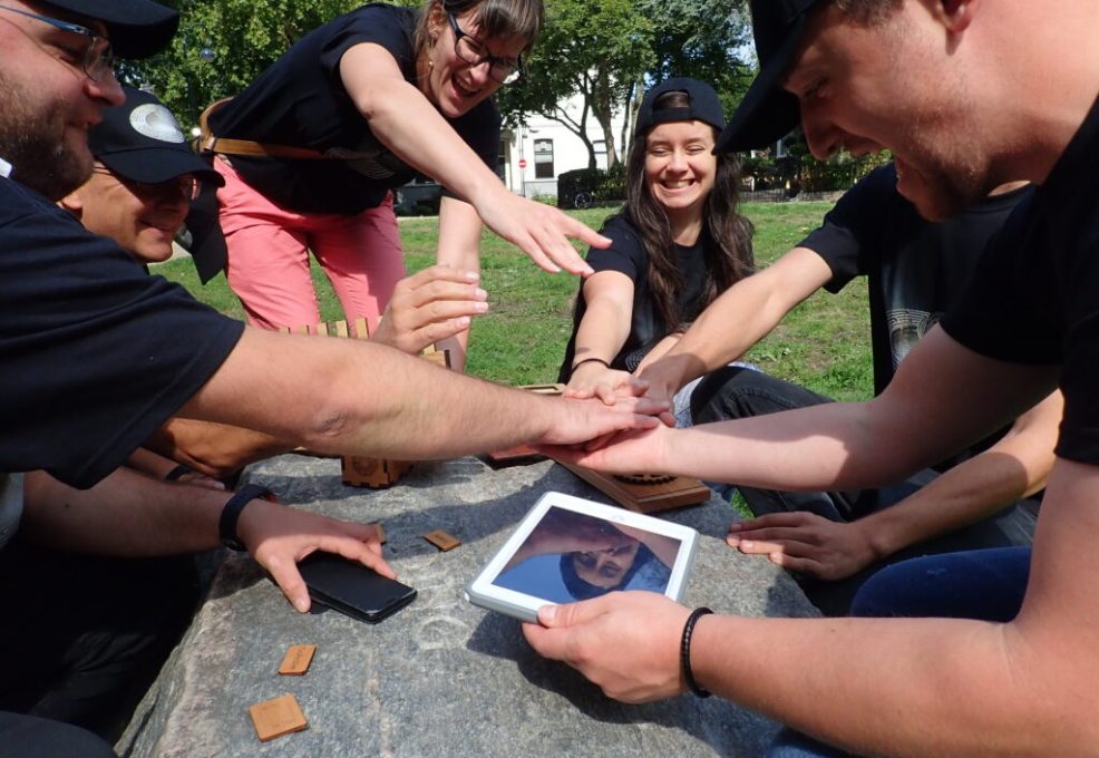 A group of participants enthusiastically working together on a tablet during the Sleuth: The Murder Mystery Scavenger Hunt team building event.