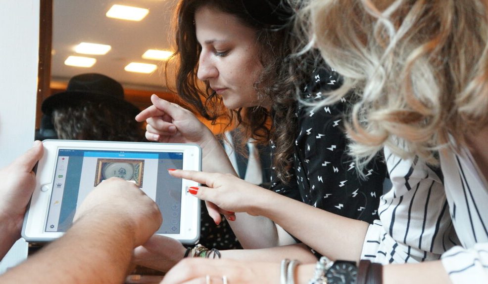 Participants closely examining clues on a tablet during the Sleuth: The Murder Mystery Scavenger Hunt team building event.
