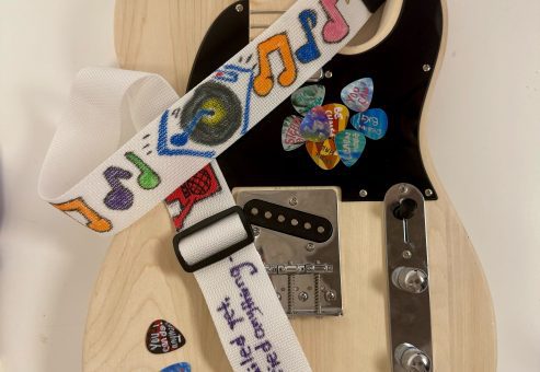 This is a nicely decorated guitar with symbols and an inspirational quote after teams have worked on it during the Charity Guitar Build team building event.