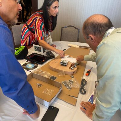 Team members discuss and organize guitar parts during the Charity Guitar Build team building event, preparing to assemble instruments for donation. thumbnail