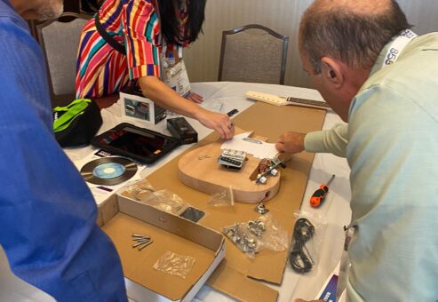Team members discuss and organize guitar parts during the Charity Guitar Build team building event, preparing to assemble instruments for donation.