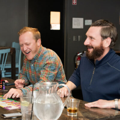 Two team members laugh together while participating in an engaging board game at a team building networking event. thumbnail