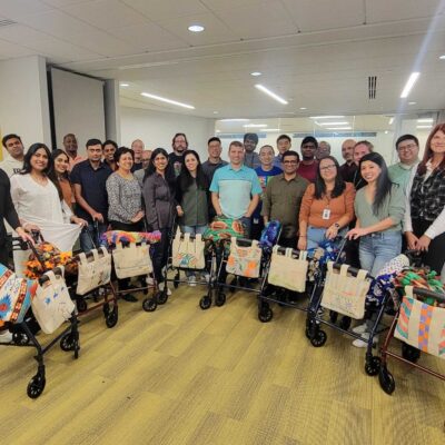 Group of participants posing with completed rollator walkers decorated with colorful blankets and tote bags, smiling after the successful assembly during a charitable team building program. thumbnail