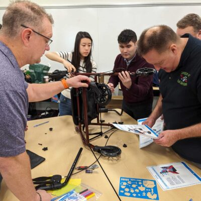 Group of participants assembling a rollator walker, following instructions from a manual during a charitable team building event. thumbnail