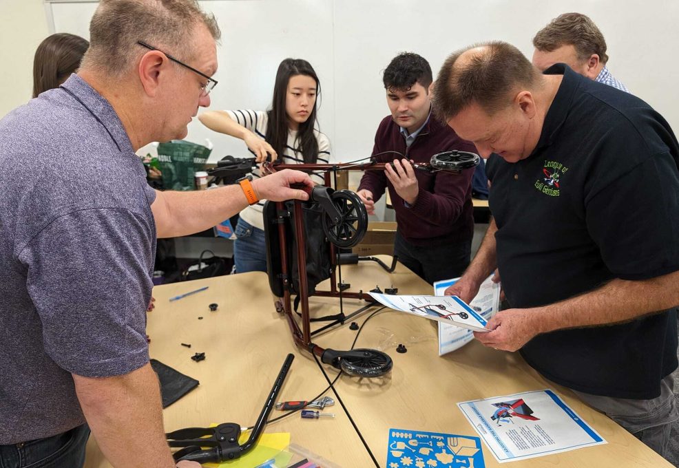Group of participants assembling a rollator walker, following instructions from a manual during a charitable team building event.