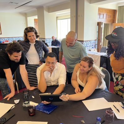 Team building activity focused on human skills training. A group gathers around a tablet, collaborating and strategizing to complete a challenge, reinforcing teamwork, communication, and problem-solving skills. thumbnail