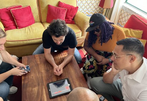 Team building activity focused on human skills training. A group collaborates around a tablet, strategizing and problem-solving to complete a challenge, emphasizing teamwork and critical thinking.