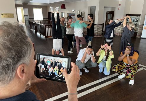 Interactive team building activity focused on human skills training. Participants form creative group poses while a teammate captures the moment, emphasizing collaboration, communication, and teamwork in a fun learning environment.
