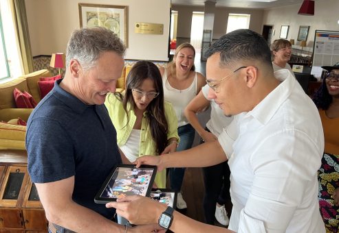 Team building activity focused on human skills training. Participants review their challenge results on a tablet, celebrating teamwork, creativity, and collaboration in an engaging learning experience.
