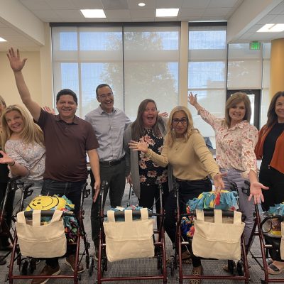 diverse group of eight adults joyfully posing behind their assembled rollator walkers, each adorned with a colorful fleece and a personalized accessory bag, showcasing their collaborative effort in a well-lit room. thumbnail