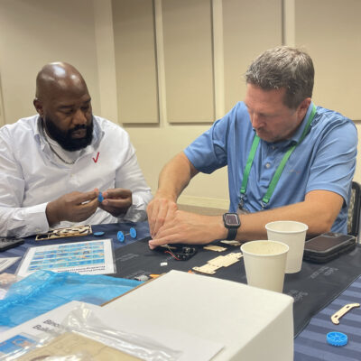 Two participants working together at a table to assemble components of a STEM project during the STEM Speedway team building activity, highlighting collaboration, problem-solving, and hands-on learning. thumbnail
