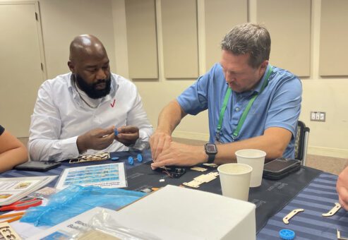 Two participants working together at a table to assemble components of a STEM project during the STEM Speedway team building activity, highlighting collaboration, problem-solving, and hands-on learning.