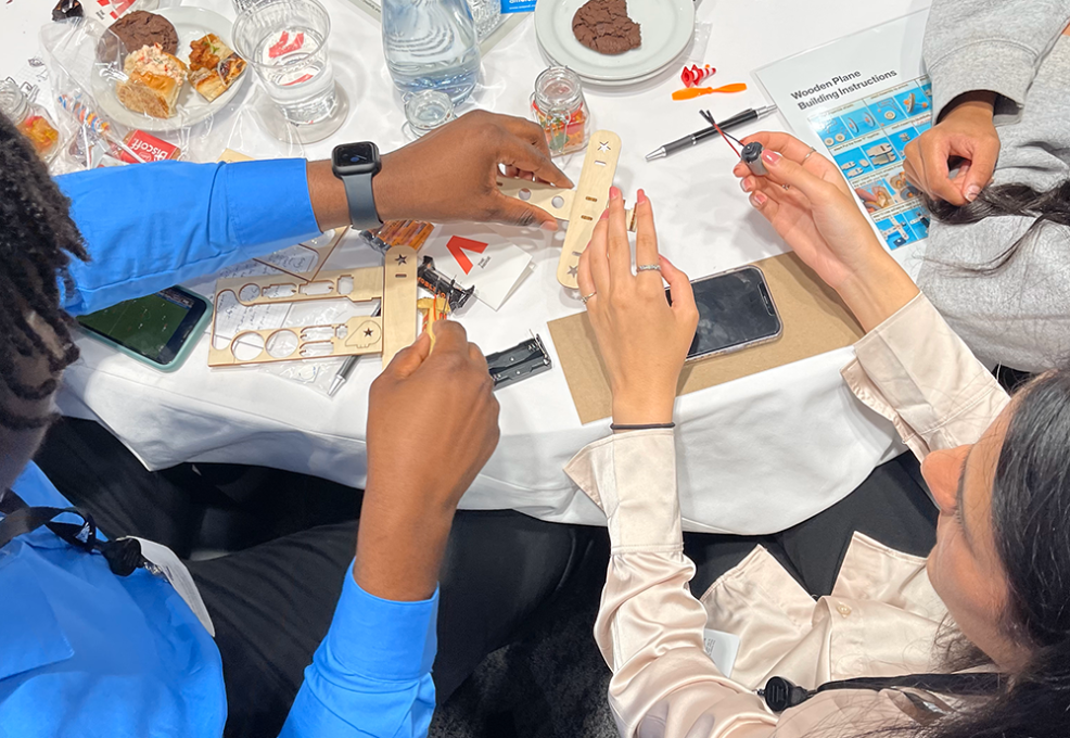 Participants working together at a table, assembling parts of a miniature airplane from a STEM kit during the STEM Speedway team building activity, focusing on teamwork, precision, and hands-on learning.