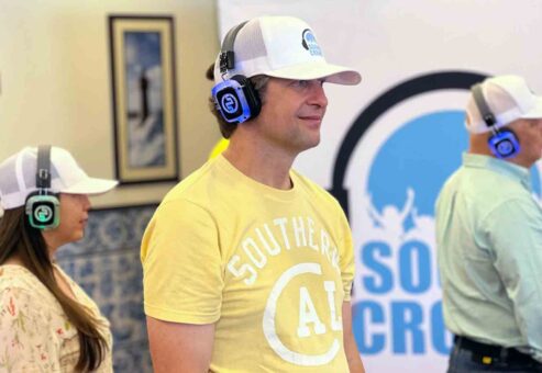 A group of participants in a Sound Crowd event stand attentively while wearing noise-cancelling headphones. They are participating in a team building event that focuses on non-verbal communication.