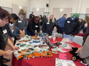 A group of people is engaged in a crafting activity at tables, working on a colorful blanket project.