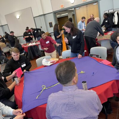 Team members collaborate on crafting a fleece blanket during a charitable team building event, contributing to donations for a good cause as part of the Hope for the Holidays program. thumbnail
