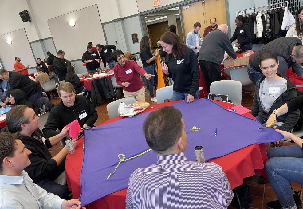 Team members collaborate on crafting a fleece blanket during a charitable team building event, contributing to donations for a good cause as part of the Hope for the Holidays program.