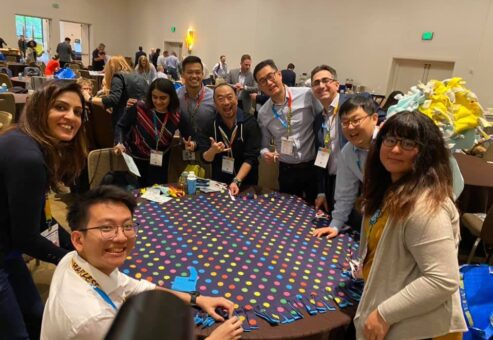 A group of colleagues enjoys the team building experience at the Hope for the Holidays event, working together to assemble colorful blankets for donation to local seniors during the holiday season.