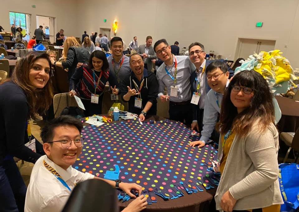A group of colleagues enjoys the team building experience at the Hope for the Holidays event, working together to assemble colorful blankets for donation to local seniors during the holiday season.
