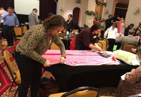 Participants at the Hope for the Holidays team building event work together to craft personalized blankets, spreading warmth and cheer to local seniors during the festive season.