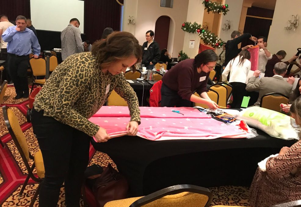 Participants at the Hope for the Holidays team building event work together to craft personalized blankets, spreading warmth and cheer to local seniors during the festive season.
