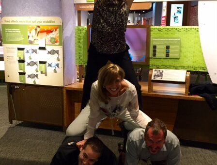 Team members forming a human pyramid during a museum scavenger hunt. This collaborative activity promotes teamwork, fun, and creativity while solving clues and engaging with interactive exhibits.