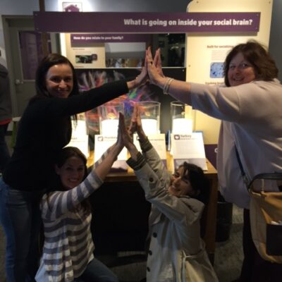 Team members collaborating in a museum exhibit during a scavenger hunt. They engage in a hands-on challenge, using teamwork to explore and solve interactive brain teasers. thumbnail