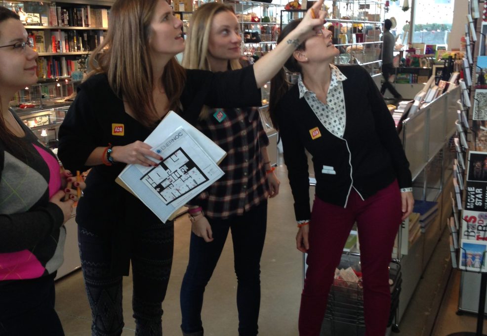 Team members collaborating during a museum scavenger hunt, engaging with a colorful art piece while solving clues. The activity fosters teamwork, creativity, and exploration in an interactive setting.