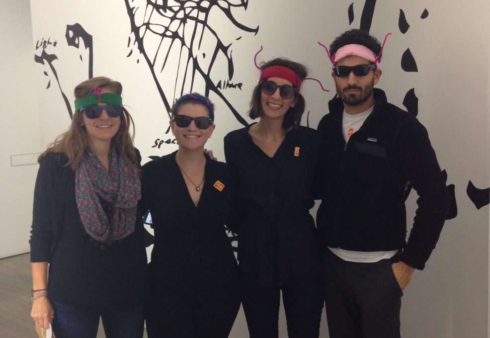 Team members in creative costumes during a museum scavenger hunt. Wearing fun glasses and engaging with an art exhibit, they work together to solve clues in this interactive team building activity.