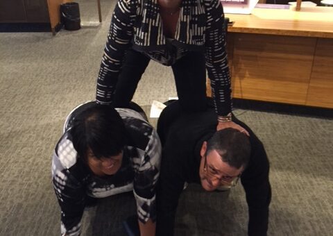 Team members forming a human pyramid during a museum scavenger hunt. This activity encourages teamwork, collaboration, and creative problem-solving while engaging with interactive exhibits.