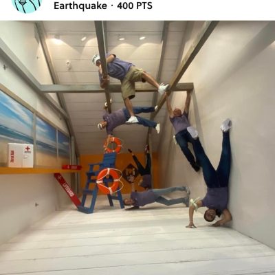 Team Mint posing creatively in an upside-down earthquake exhibit during a museum scavenger hunt. This team building activity promotes problem-solving, collaboration, and interactive fun in a unique setting. thumbnail