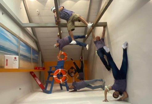 Team Mint posing creatively in an upside-down earthquake exhibit during a museum scavenger hunt. This team building activity promotes problem-solving, collaboration, and interactive fun in a unique setting.