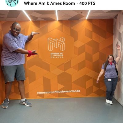 Team Pink posing in the Museum of Illusions' Ames Room during a scavenger hunt. The optical illusion creates a fun challenge, enhancing teamwork and creativity as they engage in the interactive exhibit. thumbnail