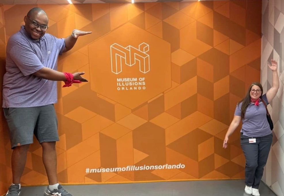 Team Pink posing in the Museum of Illusions' Ames Room during a scavenger hunt. The optical illusion creates a fun challenge, enhancing teamwork and creativity as they engage in the interactive exhibit.