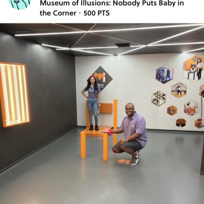 Team Pink posing in the Museum of Illusions' 'Nobody Puts Baby in the Corner' exhibit during a scavenger hunt. The optical illusion creates a fun and interactive challenge for the team to explore and solve. thumbnail