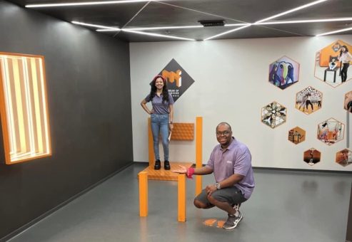 Team Pink posing in the Museum of Illusions' 'Nobody Puts Baby in the Corner' exhibit during a scavenger hunt. The optical illusion creates a fun and interactive challenge for the team to explore and solve.