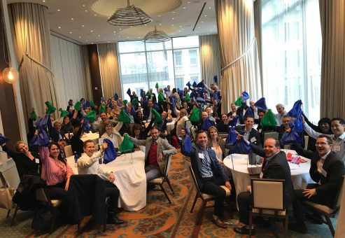 Team members posing with colorful bags during the Team Disaster Relief event. Participants work together to assemble disaster relief care kits, bonding over fun challenges that foster teamwork and communication.